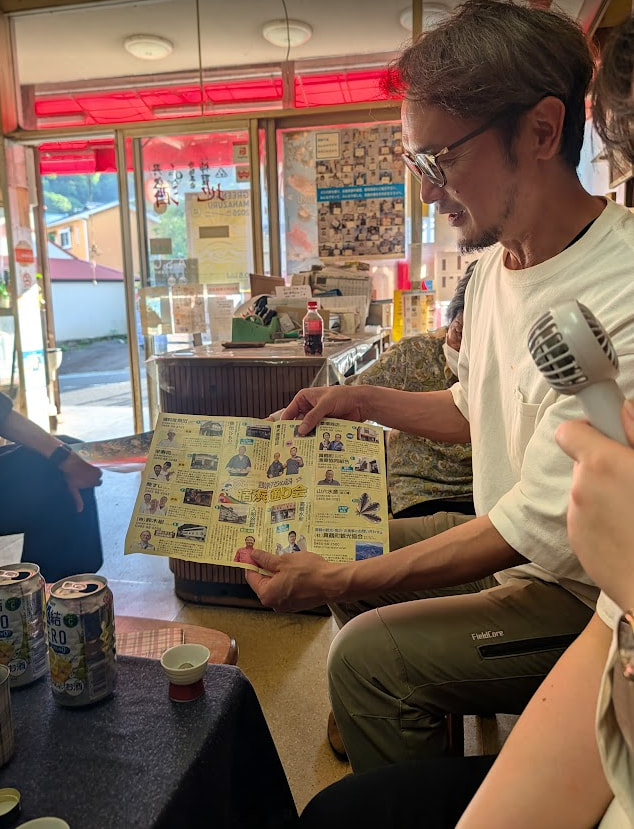 kusayanagi-shoten-manazuru-community-dialogue 100年続く真鶴町の老舗「草柳商店」の店内で、地域のパンフレットを広げて対話や交流を楽しむ様子。