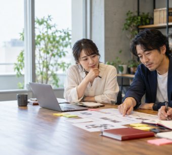 オフィスで資料やPCを見ながら業務プロセスを議論するチーム